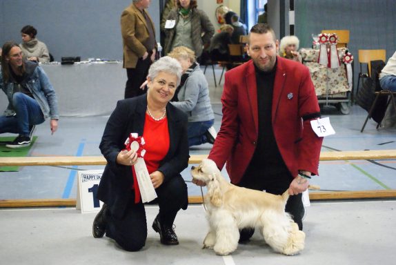 Eine Frau und ein Mann posieren mit einem Hund und mehreren Auszeichnungen.